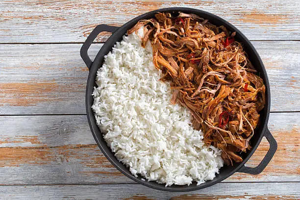 pulled slow-cooked pork shoulder grilled in oven with basmati rice in iron frying pan on wooden table, view from above