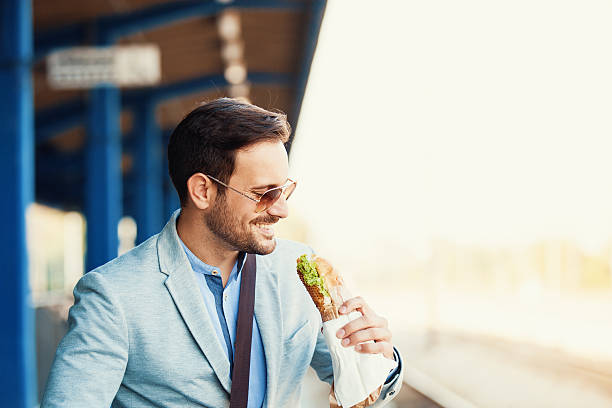 Young businessman is eating sandwich while waiting train.