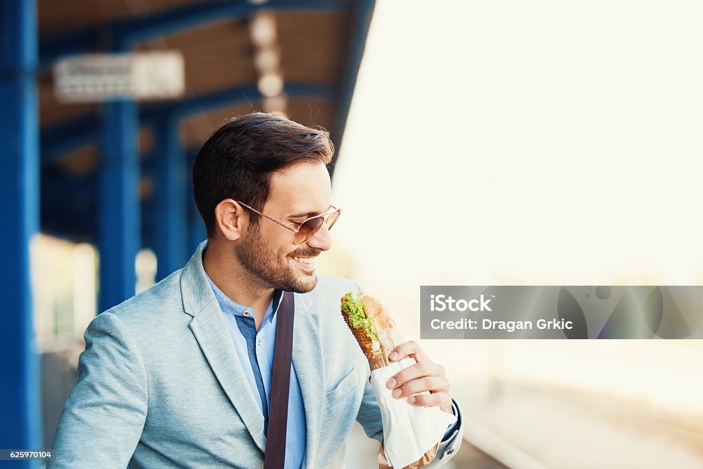 Businessman on rail station Young businessman is eating sandwich while waiting train. Eating Stock Photo