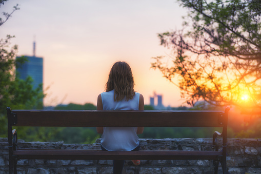 Girl sitting on a bench and watching distant city scenic.