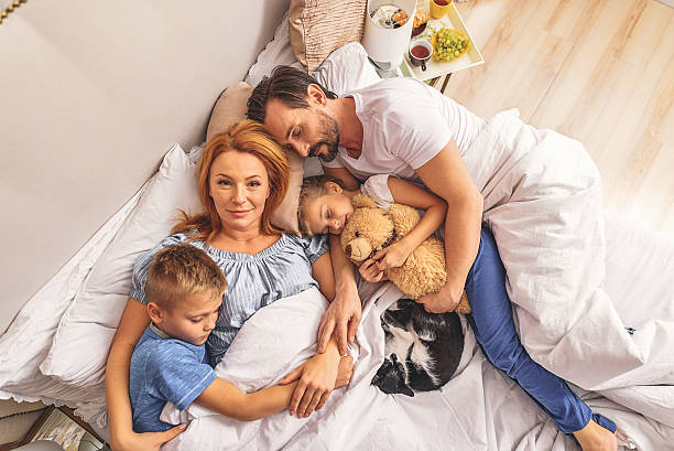 Loving family sleeping together I am very happy. Top view of joyful adult mother lying on bed and looking at camera. Father and children sleeping beside her man with teddy bear stock pictures, royalty-free photos & images