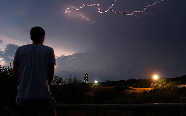 Man sitting on the fence watching lightning strike stock photo
