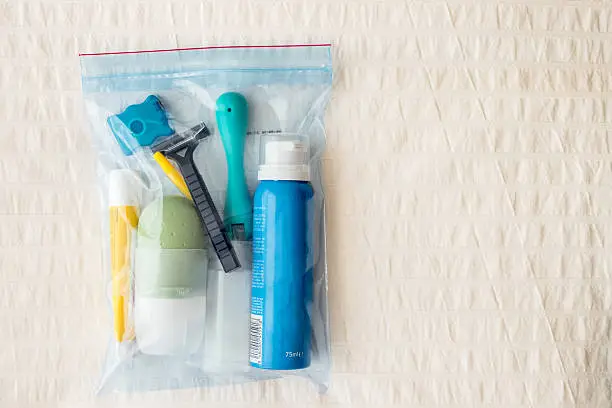 Bag of airplane items ready to be tucked into the suitcase. Liquids in containers less than 100 ml. Bag on the bedspread.
