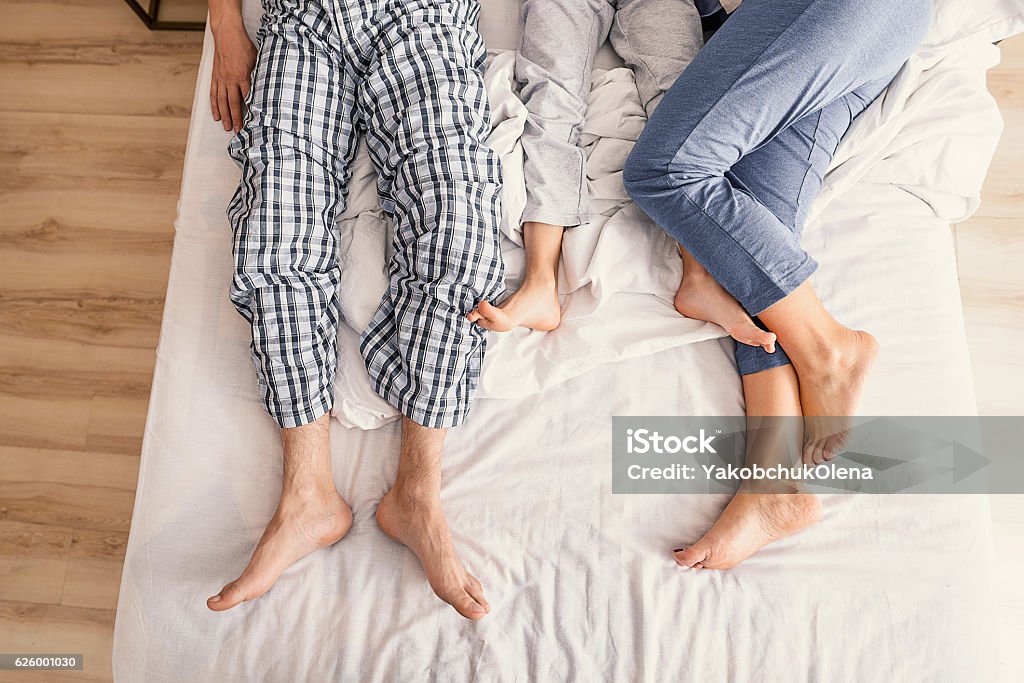 Parents and kid enjoying themselves after waking up Love makes family. Top view of father, mother and their son in pajamas showing their feet on bed Family Stock Photo