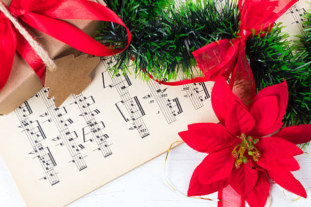 Christmas ornament and music sheet on white natural wooden table Christmas ornament and music sheet on white natural wooden table. Red ribbon bow. Poinsettia. Gift or present with label and twine. religious christmas greetings stock pictures, royalty-free photos & images