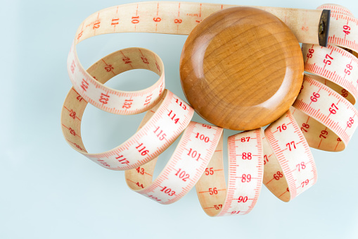 Yo-yo effect in diet concept. Wooden yoyo with centimeter measure. Flat lay top view. Reflective glass background. Copy space in the bottom left corner.