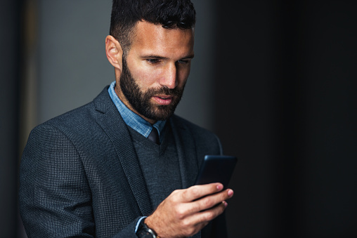Side view of a young businessman texting on the cellphone.