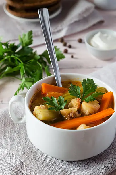 A close-up of a bowl of fish soup with carrots, celery and parsley