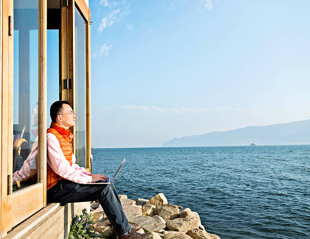 Young man working on his laptop while sitting by the lake.