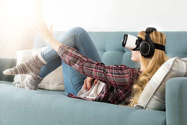 istock Woman wearing virtual reality goggles and lying on a couch. 626073012