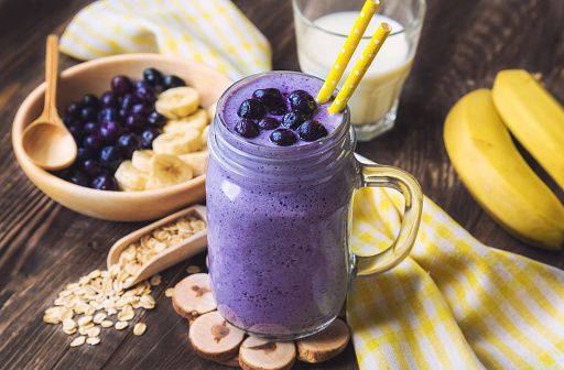 Blueberry smoothie with banana and oat flakes in jar on rustic wooden background.