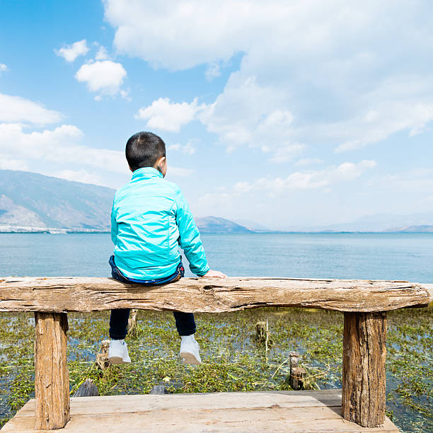 istock Little asian boy sitting on lakeside jetty 626076256