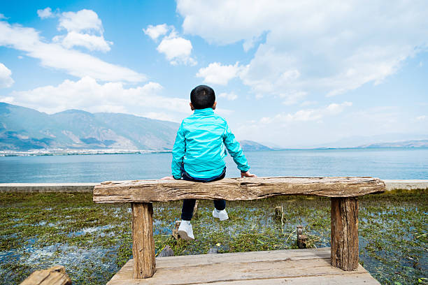 istock Little asian boy sitting on lakeside jetty 626076380