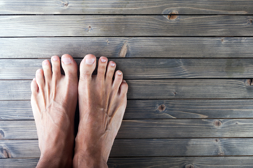 Stock photo showing close-up view of man's feet crossed at ankles on wooden table.