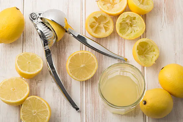 A lemon press surrounded by whole lemons, sliced lemons, squeezed lemons halves, and lemon juice in glass on a wooden surface.