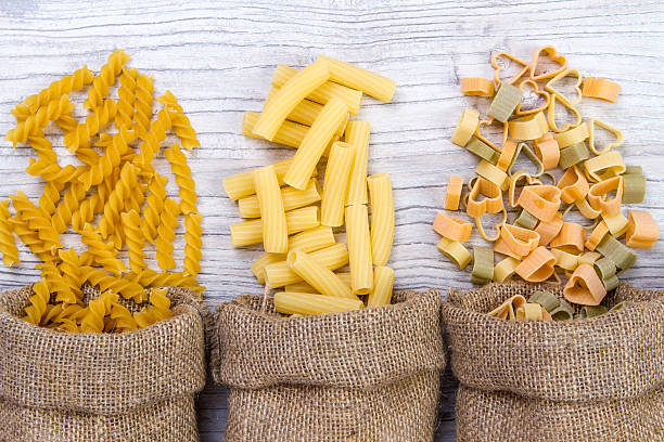 combinations of pasta in  bags of burlap on wooden background Various mix of pasta on wooden rustic background, sack. Diet and food concept. diversity carbohydrate food type photos stock pictures, royalty-free photos & images