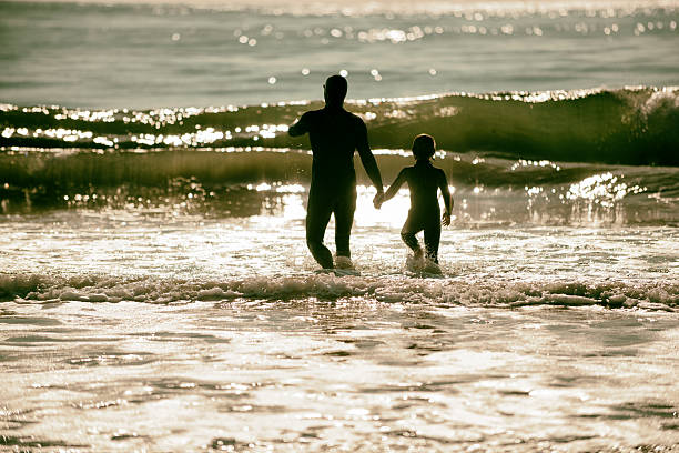 Father and son walking into surf in beautiful ocean