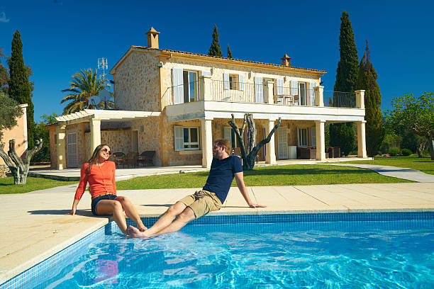happy couple sitting at pool of rural estate young couple enjoying first warm days of spanish spring at swimming pool of their finca house mallorca couple retreat stock pictures, royalty-free photos & images