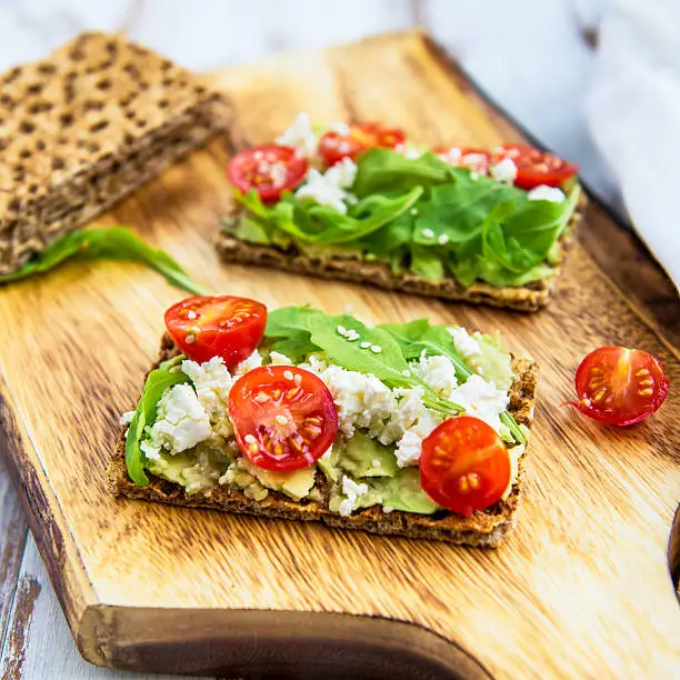 Healthy Snack from  Wholegrain Rye Crispbread Crackers with Avocado, Cherry Tomatoes, Rocket Salad and Goat Cheese