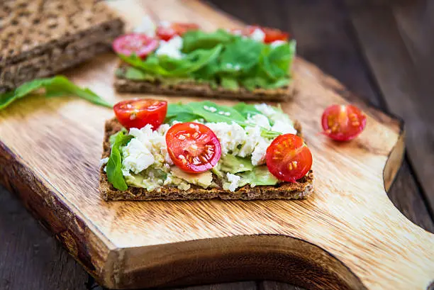 Healthy Snack from  Wholegrain Rye Crispbread Crackers with Avocado, Cherry Tomatoes, Rocket Salad and Goat Cheese