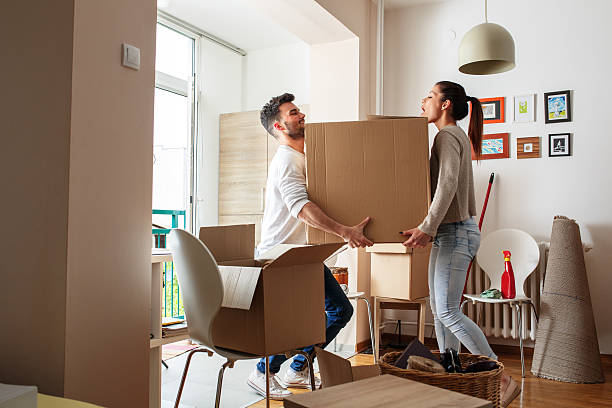 Moving house Young couple carrying big cardboard box at new home.Moving house. unpacking photos stock pictures, royalty-free photos & images
