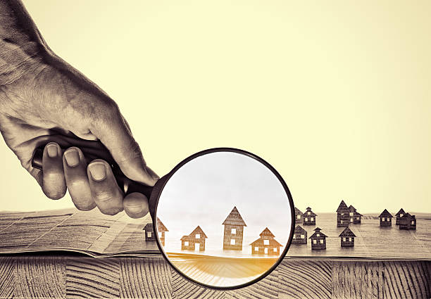Paper house under a magnifying lens Hand holds the magnifying glass in front of an open newspaper with paper houses. That could mean rent, search, purchase real estate. real estate office photos stock pictures, royalty-free photos & images