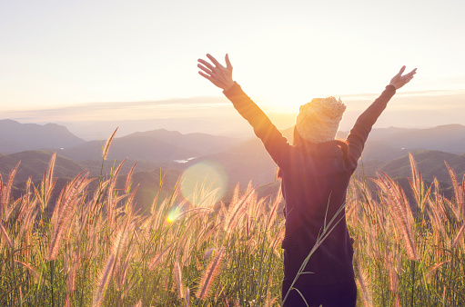 Carefree Happy Woman Enjoying Nature on grass meadow on top of mountain cliff with sunrise. Beauty Girl Outdoor. Freedom concept. Len flare effect. Sunbeams. Enjoyment.