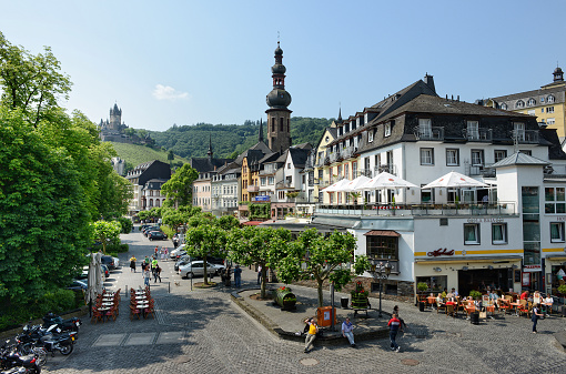 Cochem, Germany - June 2, 2014: Cityscape of Cochem at Moselle river in summer. People sitting in bars and restaurants on market place. bikes parking. people sitting on a bench. (Rhineland-Palatinate, Germany)