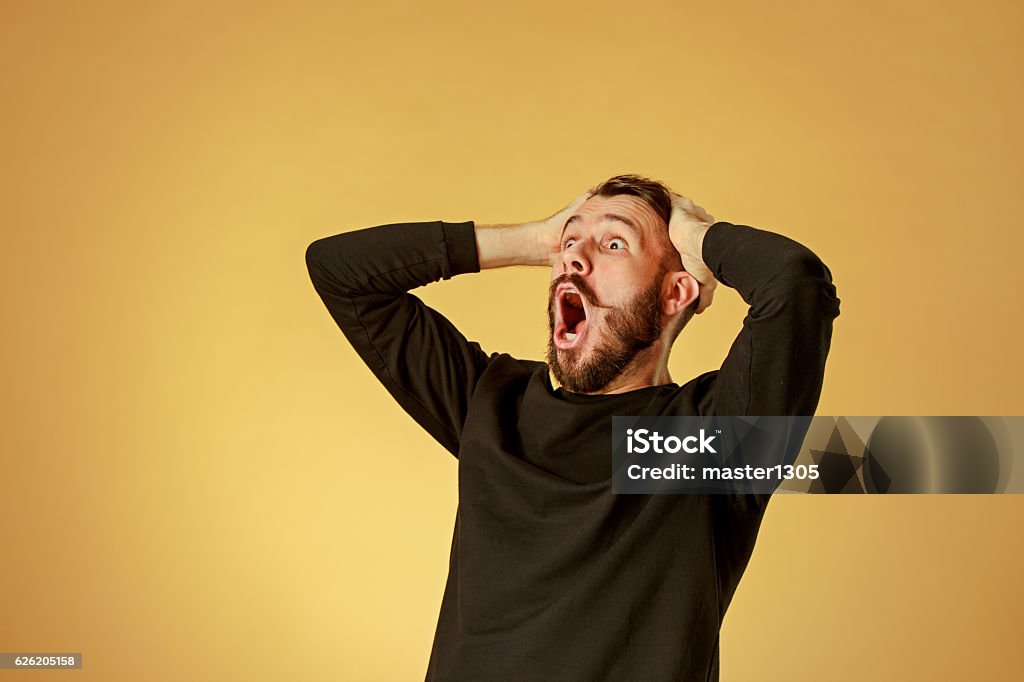 Portrait of young man with shocked facial expression Portrait of young man with shocked facial expression over orange studio background Surprise Stock Photo