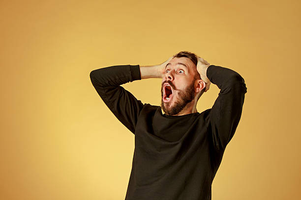 Portrait of young man with shocked facial expression Portrait of young man with shocked facial expression over orange studio background ecstasy stock pictures, royalty-free photos & images