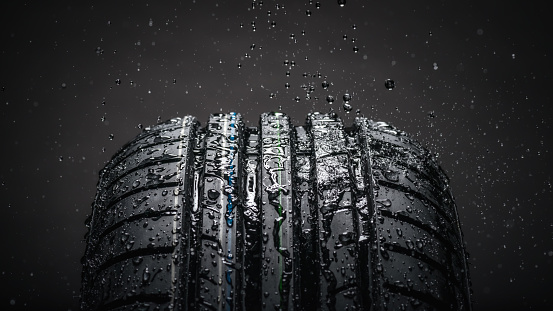 Close-up on Brand new, high performance wet winter symmetrical tire Dunlop SP Sport Blueresponse. Water splashing on during the rain. Black background.