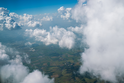 Earth landscape viewed from airplane. Earth surface under the white clouds and blue sky from aerial view. Cloudy weather covering residential land and argriculture land.