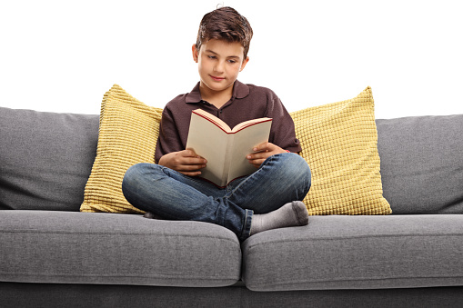 Boy sitting on a sofa and reading a book isolated on white background