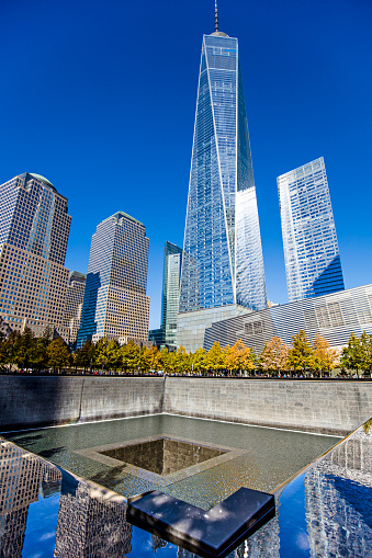 People visiting the  September 11 Memorial with One World Trade Center in the background.