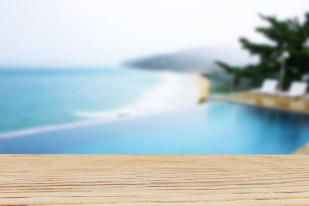 istock Wooden table top on blurred pool and beach background 626242282