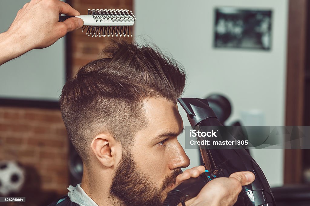 The hands of young barber making haircut to attractive man The hands of young barber making haircut of attractive bearded man in barbershop Men Stock Photo