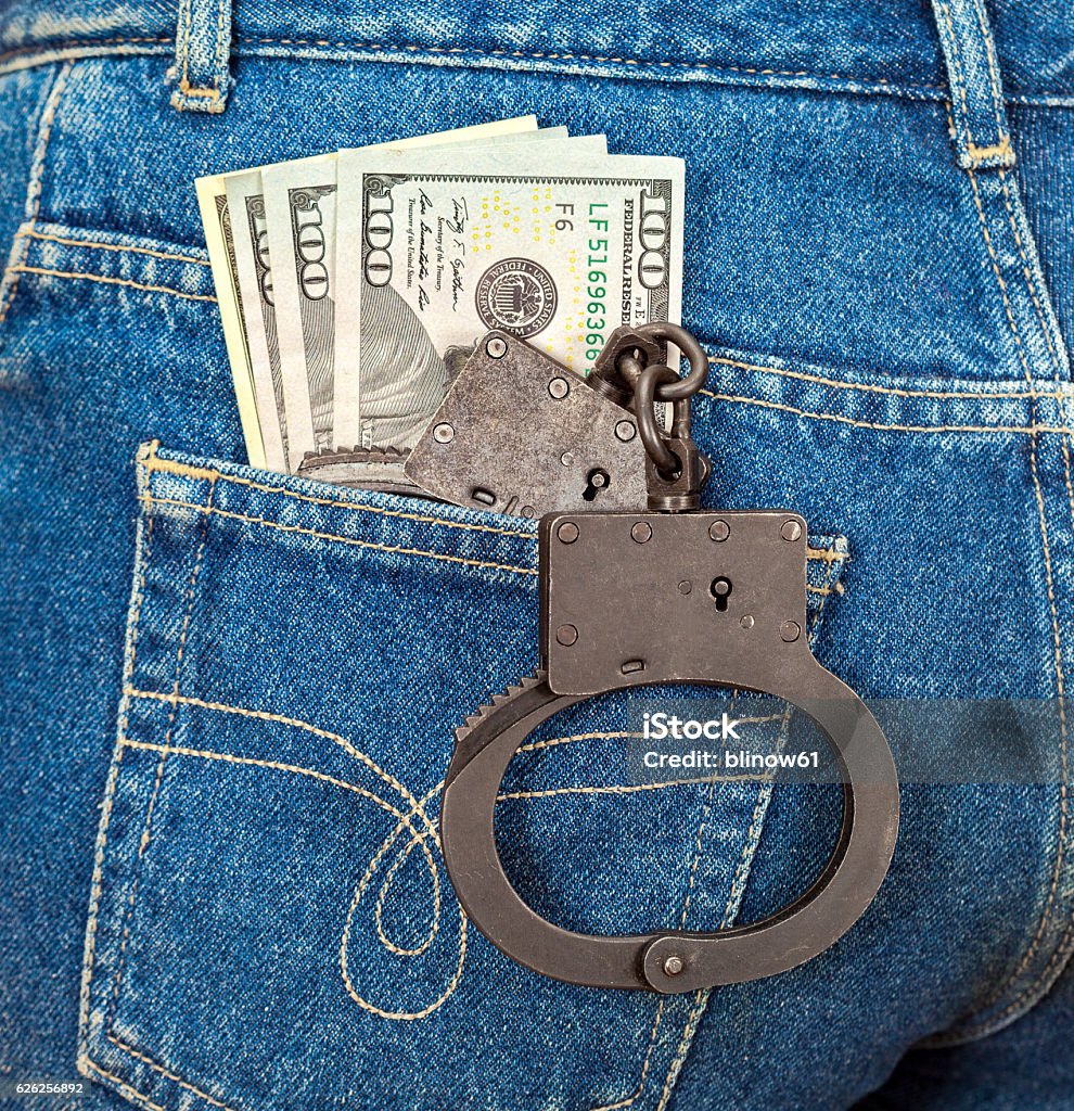 Black metal handcuffs and american currency in back jeans pocket Arrest Stock Photo