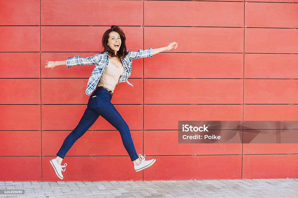 Jumping happy girl Excited girl is jumping against a red wall One Woman Only Stock Photo