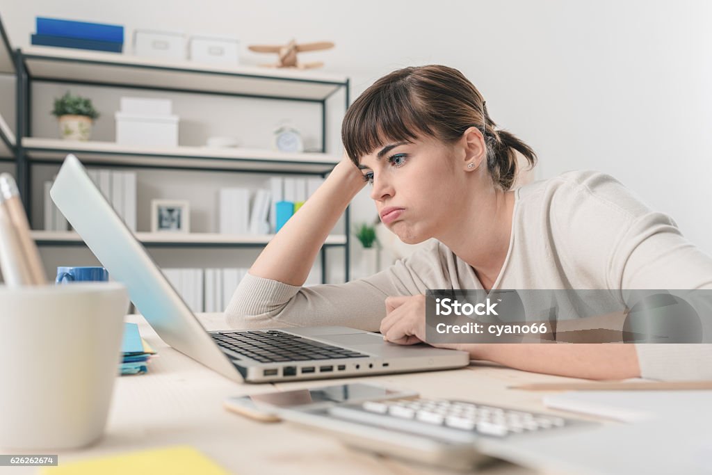 Disappointed woman working with a laptop Tired disappointed woman working at office desk with a laptop, connection and computer problems concept Slow Stock Photo