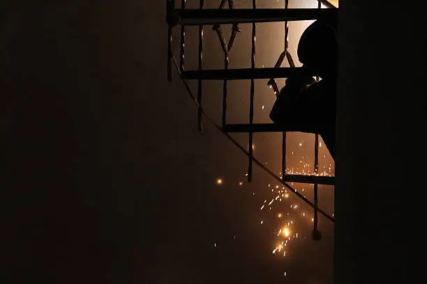Welder produces sparks as he repairs an iron spiral staircase. Sparks fly as this craftsman repairs a damaged spiral staircase in a home.
