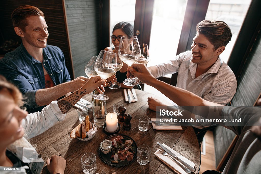 Young friends toasting wine at cafe Group of men and women enjoying wine at restaurant. Young friends toasting wine at cafe. Celebratory Toast Stock Photo