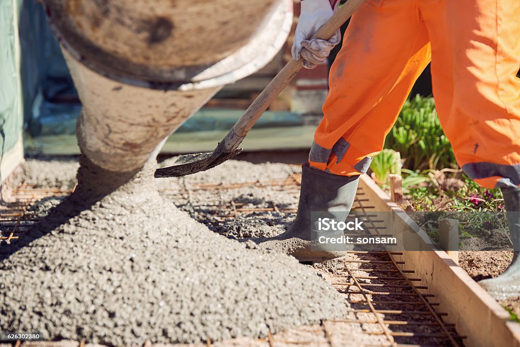 Concrete pouring during commercial concreting floors of building Worker with gum boots spreading ready mix concrete Concrete Stock Photo