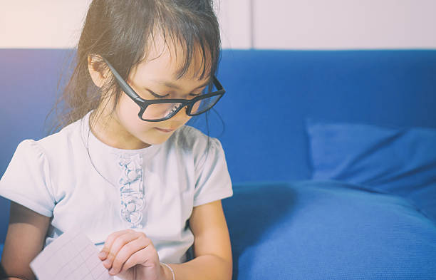 istock Nerdy Asian child is reading a book on a sofa 626305494
