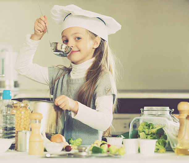 istock Smiling female child in chef cap making bouillon in kitchen 626310824