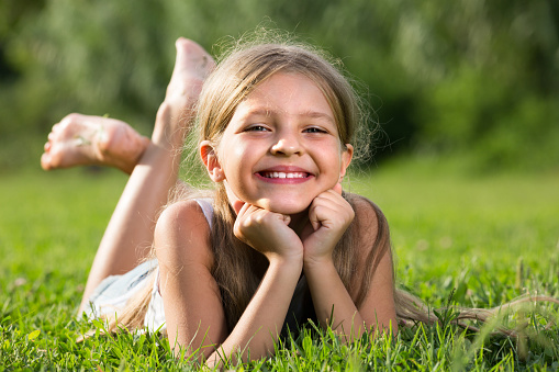 ï»¿portrait of smiling girl in lying on grass in park and looking happy
