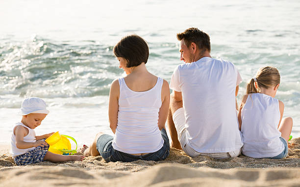 istock back view on family of four sitting on beach 626329948