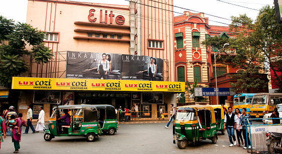 Kolkata, India - January 19, 2013: Auto rickshaw taxis and pedestrians move past the old cinema theater on January 19, 2013. Indian three-wheelers have the design of the Piaggio Ape C from 1948