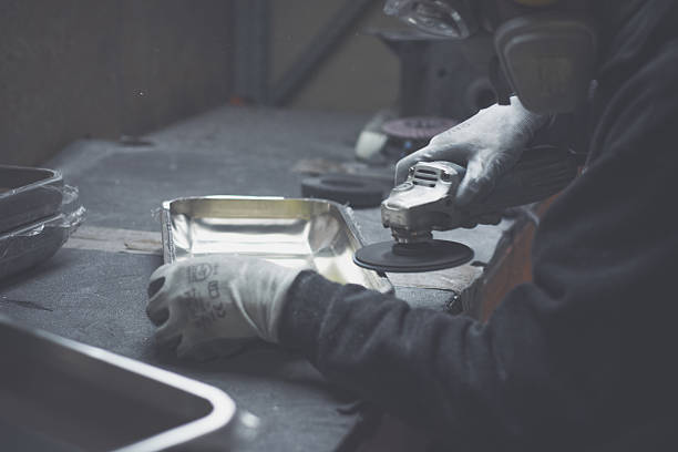 Worker polishing a stamped aluminum product with an angle grinder stock photo
