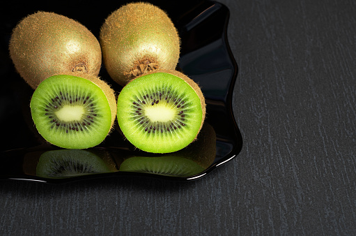 Kiwi fruit and two half in black plate on the stone table