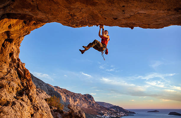 male climber gripping on handhold while climbing in cave - climbing men sea cliff imagens e fotografias de stock